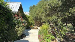 Un chemin en béton bordé d’une végétation luxuriante et de plantes en fleurs, qui mène à un bâtiment doté d’un toit en pente.