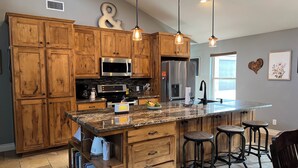 Une cuisine moderne avec des meubles en bois, des appareils en acier inoxydable, un plan de travail en granit et des luminaires suspendus.