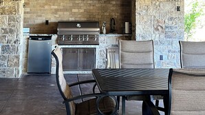 Une cuisine extérieure avec des murs en pierre, un ventilateur de plafond et un barbecue.