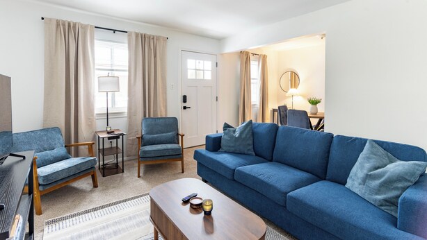 A living room with a blue sofa, two armchairs, a coffee table, and a TV. There is a door leading to another room with a lamp and a mirror. - Cute & Cozy Ferndale Duplex (Ferndale)