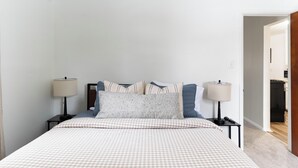 A neatly arranged bedroom with a bed, two bedside tables with lamps, and a visible doorway leading to another room. - Cute & Cozy Ferndale Duplex (Ferndale)