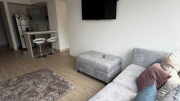 Una sala de estar moderna con un sofá gris, un reposapiés y un televisor de pantalla plana montado en la pared.