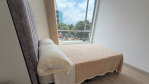 Ein Einzelbett mit beiger Bettdecke und weißen Kissen in einem Zimmer mit Holzboden und einem großen Fenster.