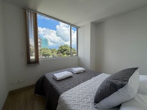 Ein Schlafzimmer mit einem Bett, einem Fenster mit Vorhängen und Blick auf Bäume und ein Gebäude.