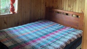 Ein Zimmer mit Holzboden, einem Bett, einem Fenster mit roten Vorhängen und einer Deckenleuchte.