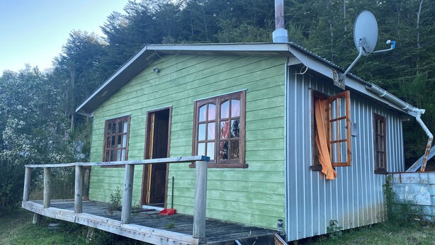 Eine kleine, eingeschossige Hütte mit Veranda, Schornstein und Satellitenschüssel.
