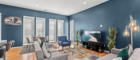 A modern living room with a blue accent wall, a grey sofa, a blue armchair, a coffee table, and a TV.