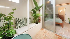 Een balkon met een zithoek, een bloempot en uitzicht op een slaapkamer met een bed en een trap.