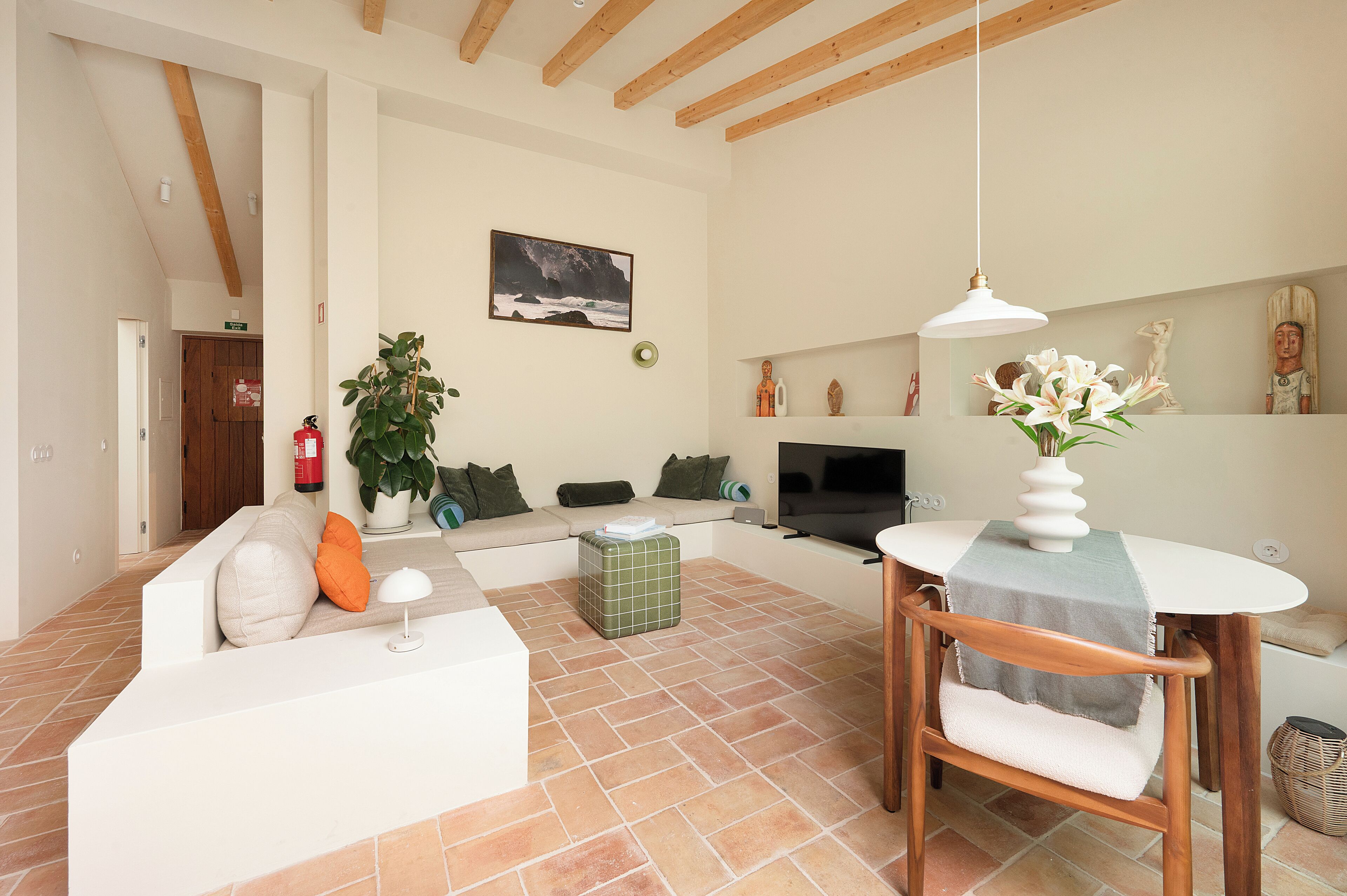 A modern living room with a sofa, a dining table, and a TV. There is a plant and a painting on the wall.