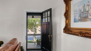 Una stanza con una porta nera che dà su uno spazio esterno, un quadro appeso al muro e una panca in pelle marrone.