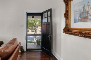 Quarto com porta preta que dá para área externa, quadro na parede e um banco de couro marrom.