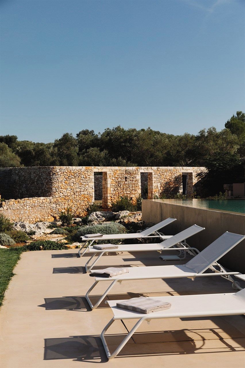 Zona de piscina con sillones de descanso y un muro de piedra.