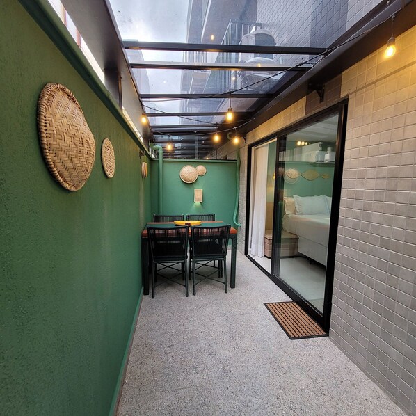 A narrow corridor with a green wall, a glass door leading to a room, and a table with chairs. - Flat Aurea Cabo Branco 50m do mar 104 (João Pessoa)