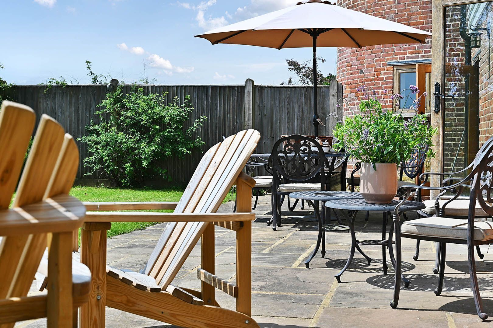 Une terrasse avec des chaises en bois, une table et un pot de fleurs.