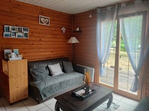 A cozy room with a wooden wall, a grey sofa, a wooden cabinet, and a table with a vase. - Chalet in a peaceful setting (Rochesson)