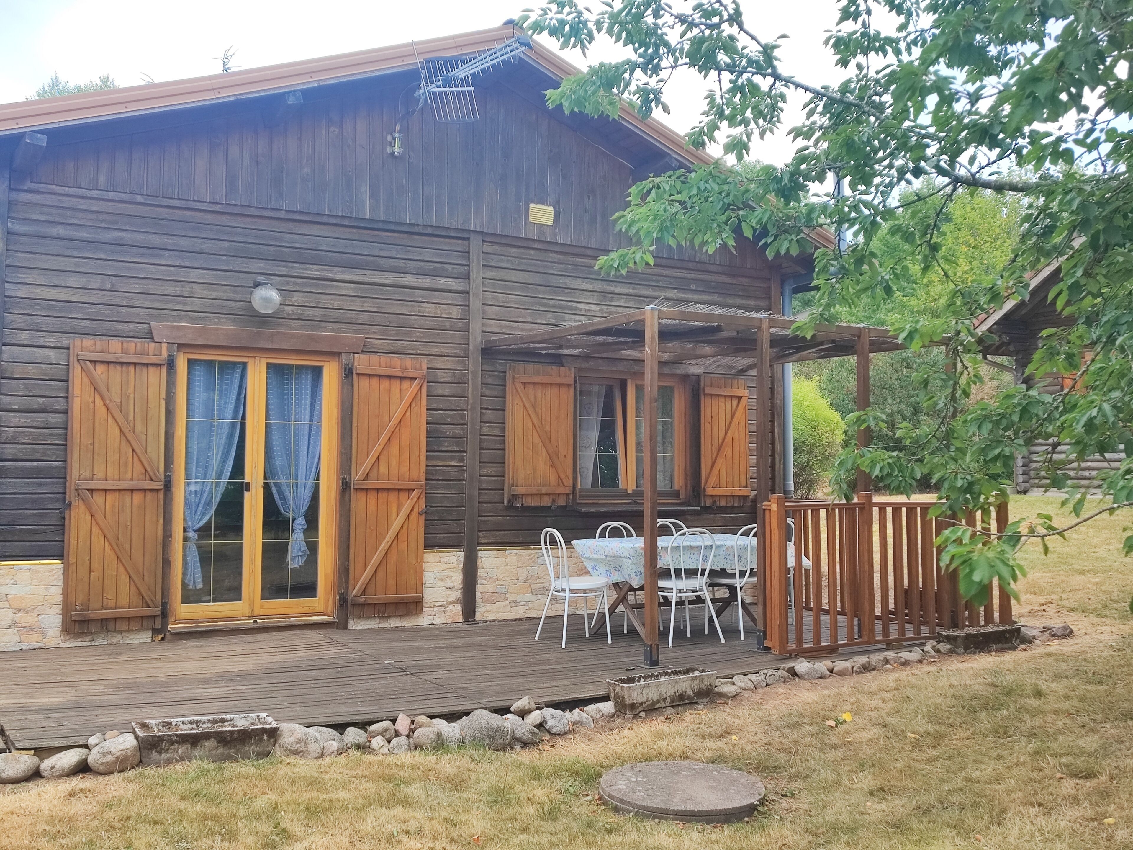 Een houten chalet met een overdekt terras, stenen muren en een houten omheining.