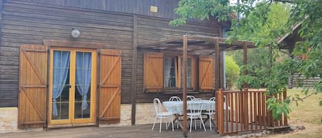 Een houten chalet met een overdekt terras, stenen muren en een houten omheining.