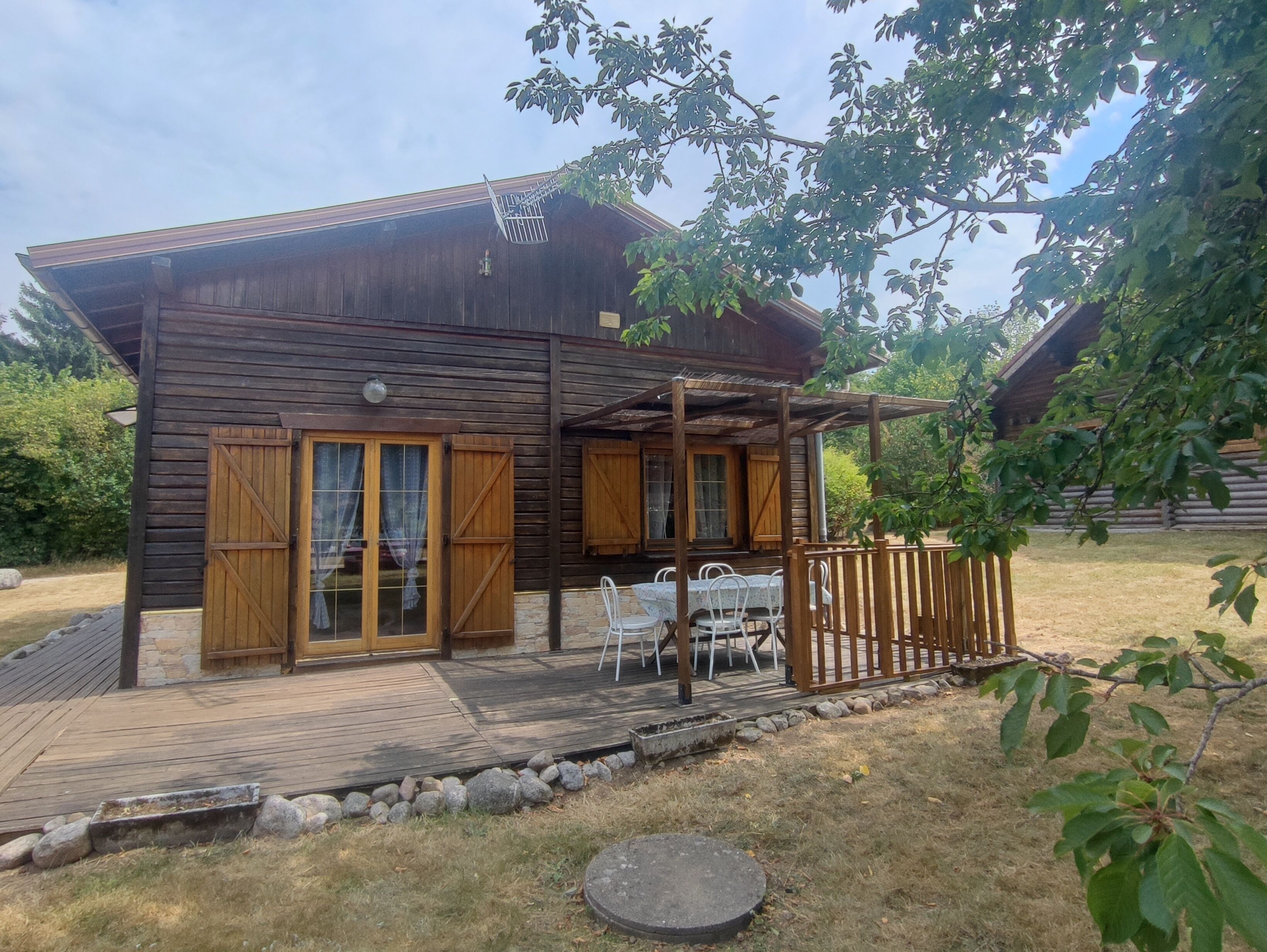 A wooden cabin with a deck, outdoor seating, and a covered patio area.