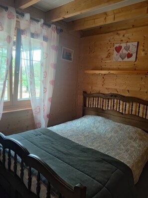 A wooden cabin room with a bed, curtains, and a wall-mounted picture. - Chalet in a peaceful setting (Rochesson)
