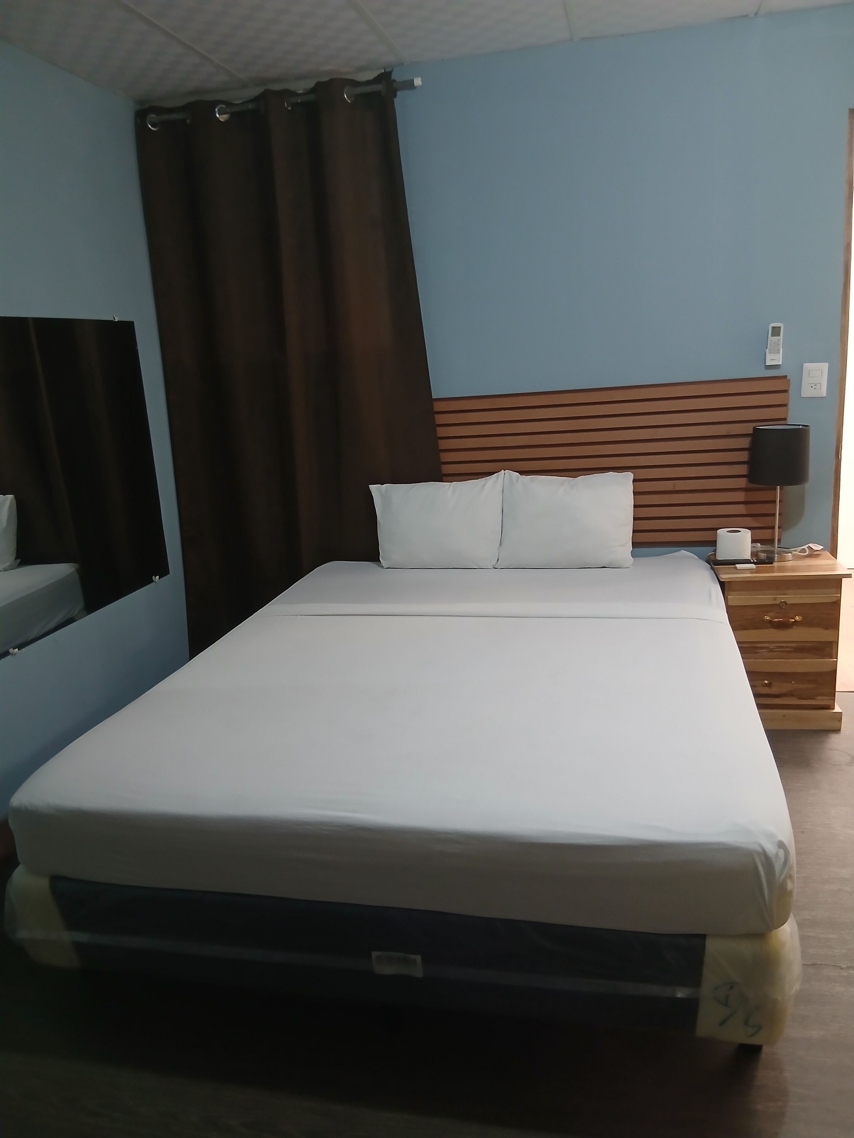Una habitación de hotel estándar con una cama, una mesita de noche, una lámpara y un espejo.