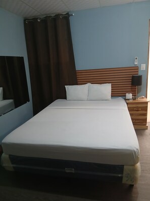 Una habitación de hotel estándar con una cama, una mesita de noche, una lámpara y un espejo.