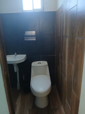 Un baño pequeño con inodoro blanco, lavamanos y una ventana sobre el lavamanos.