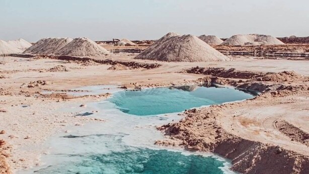 A person swimming in a clear blue pool surrounded by sand and rock formations. - Tala Villa - Dead Sea (Swemeh)