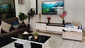 A modern living room with a flat-screen TV mounted on the wall, a sofa, a coffee table, and a side table with decorative items. - Tala Villa - Dead Sea (Swemeh)
