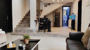 A modern living room with a black sofa, a coffee table, and a staircase leading to a dining area. - Tala Villa - Dead Sea (Swemeh)