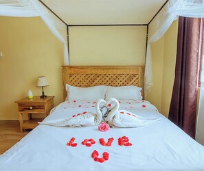 A neatly made bed with a canopy, a bedside table with a lamp, and a wall with a curtain.