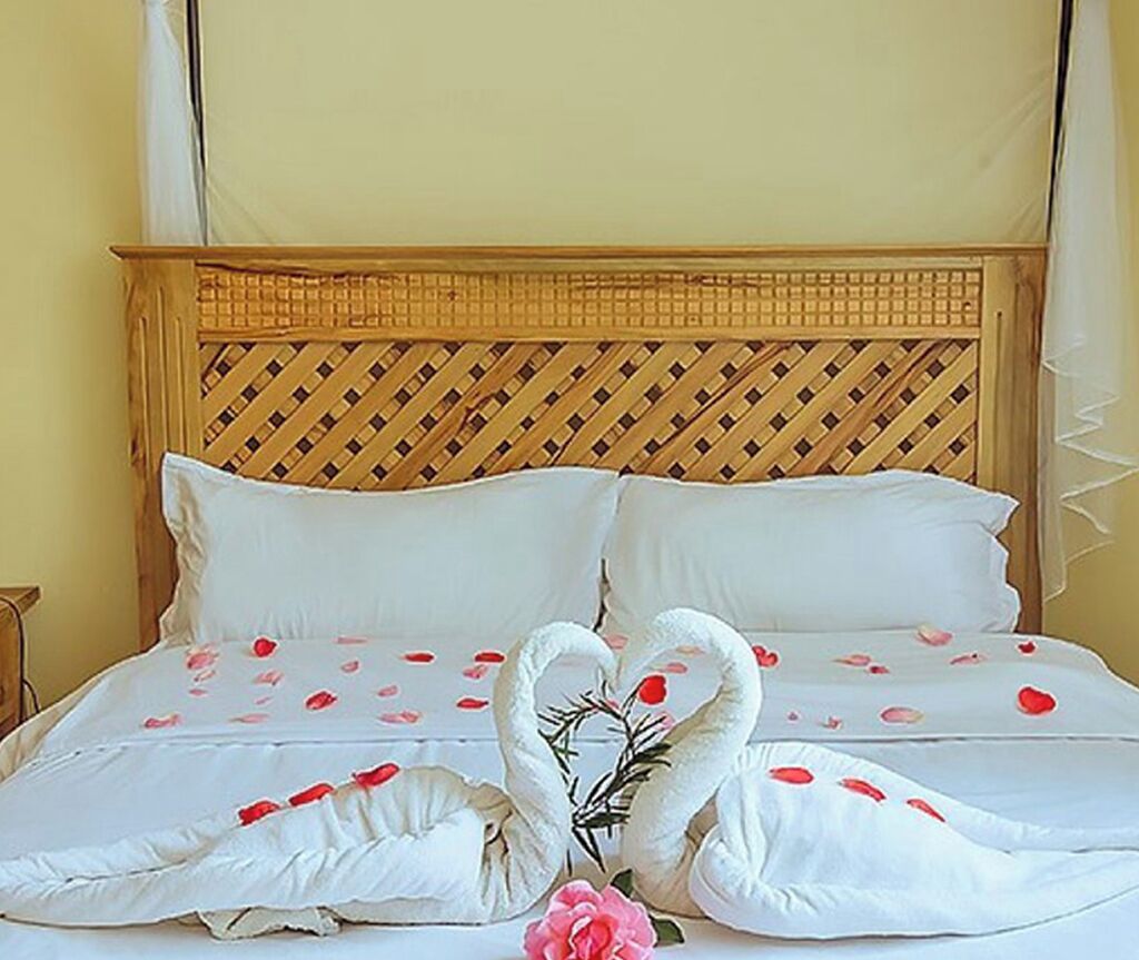 Una cama con sábanas blancas, dos almohadas y un cisne decorativo de tela.