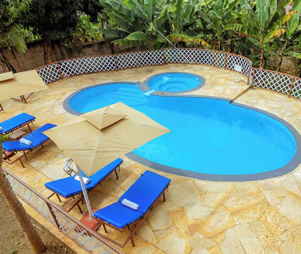 A swimming pool with a stone deck, surrounded by a lattice fence, and equipped with blue lounge chairs and umbrellas.
