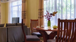 A dining area with a wooden table, chairs, and a vase of flowers. - Ngao Apartment & Suites Arusha (Arusha)