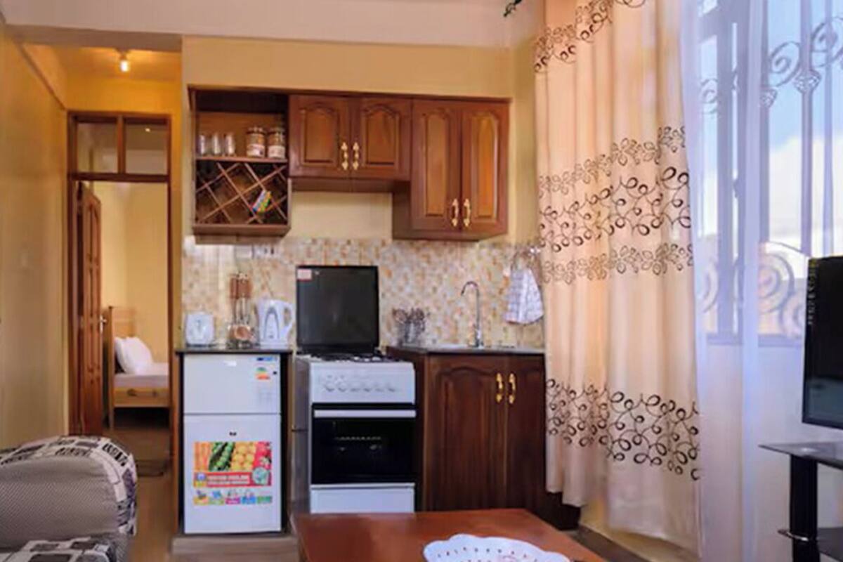 A compact kitchen with wooden cabinets, a refrigerator, a stove, and a dining table.