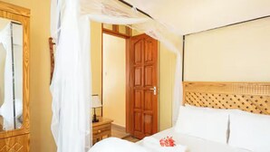 A hotel room with a canopy bed, wooden headboard, and a mirror with a wooden frame. - Ngao Apartment & Suites Arusha (Arusha)