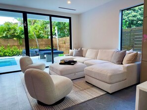A modern living room with a sectional sofa, a single armchair, and a glass door leading to a pool area. - Miami Rooftop Oasis: 4bd, 3 bath, heated pool, rooftop, firepit (Miami)