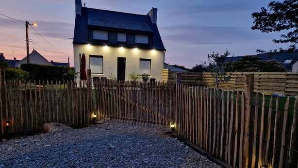 A house with a gravel driveway, wooden fence, and a well-lit entrance. - Completely renovated Breton house - Walking distance to the beach - Sleeps 8 (Penmarch)