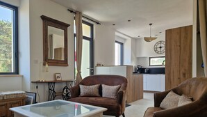 A modern living room with a glass-top coffee table, brown leather sofas, a wooden cabinet, and a kitchen area in the background. - Completely renovated Breton house - Walking distance to the beach - Sleeps 8 (Penmarch)