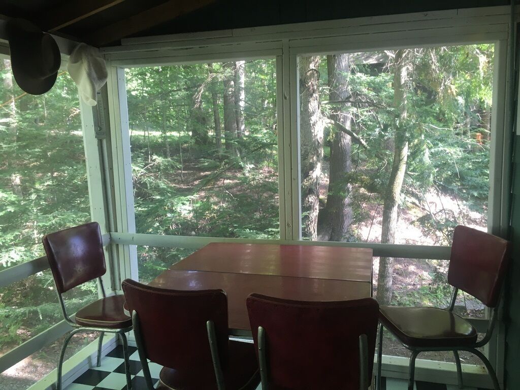Zona pranzo con tavolo e quattro sedie, ampie finestre con vista sulla foresta e pavimento a scacchi.