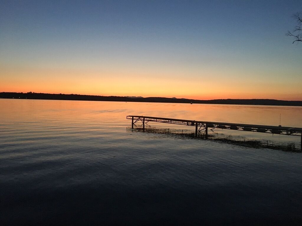 A calm lake at sunset with a dock extending into the water.