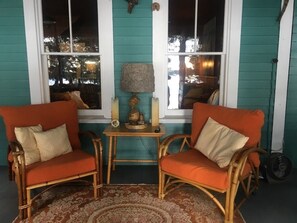 A cozy seating area with two wicker chairs and a small table, a decorative lamp, and a fan on the floor.