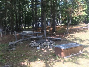 A campsite with a fire pit, picnic table, and a small wooden shed. - Classic Waterfront Maine Cottage (Madison)