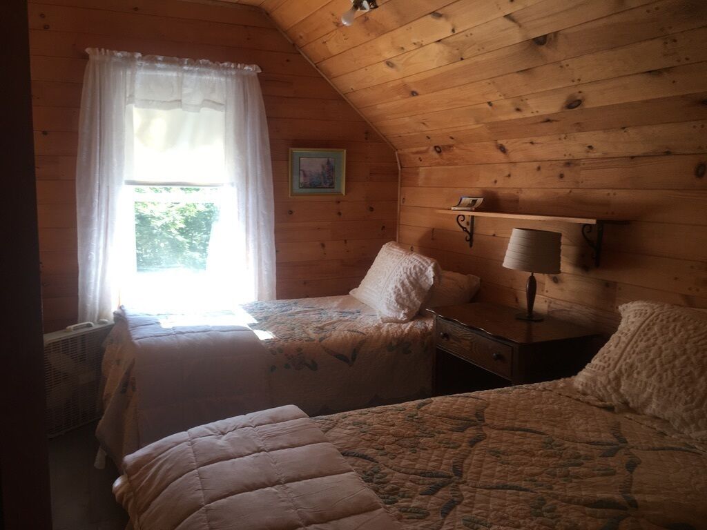 Une pièce confortable avec deux lits, un plafond en bois, une fenêtre avec des rideaux, une lampe fixée au mur et un petit tableau.
