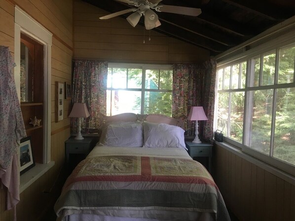 A bedroom with a bed, two bedside tables, a ceiling fan, and large windows with curtains.