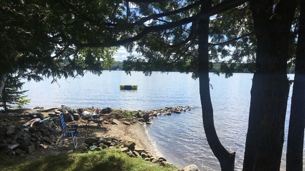 A lakeside campsite with a clear view of the water, a pile of rocks, and a blue chair.