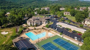 An aerial view of a residential area with a swimming pool, tennis courts, and a solar panel array. - Modern Spacious Condo with no step access, pools, fishing, games and golf! (Branson)