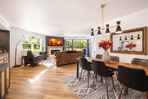 Un vaste espace de vie comprenant une cheminée, un canapé, une table à manger avec des chaises et un grand miroir.
