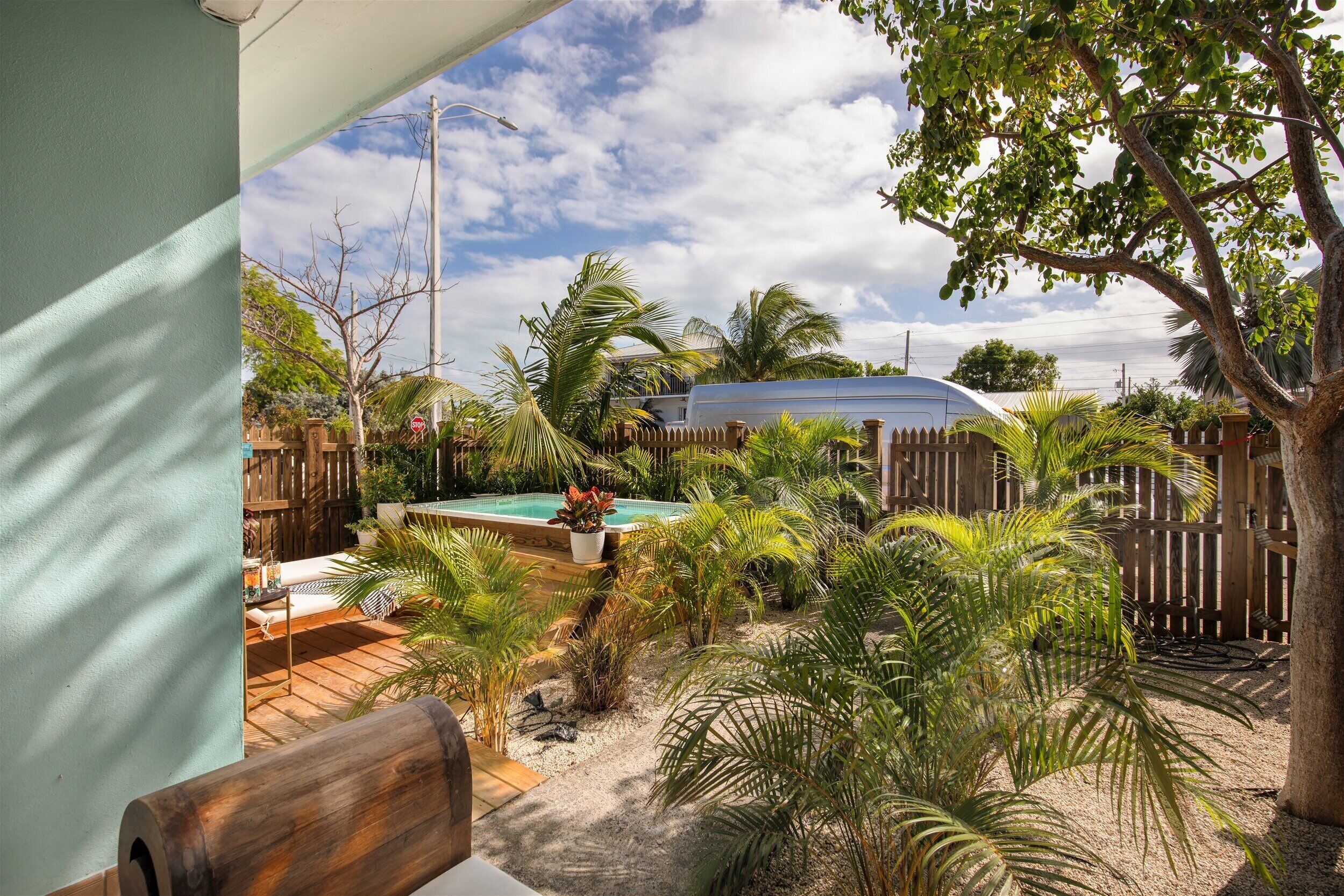 Un jardin avec une terrasse en bois, une piscine et diverses plantes tropicales.