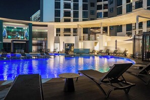 A swimming pool with lounge chairs and a table, surrounded by a building with multiple floors and balconies.