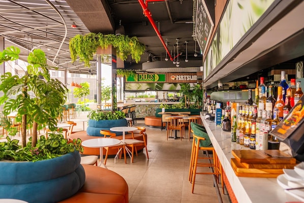 A modern cafe with indoor plants, seating areas, and a bar with various bottles.